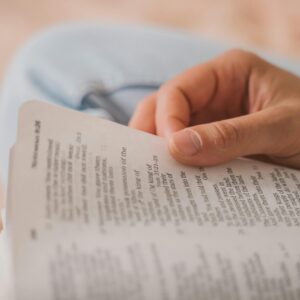 A close-up photo capturing a hand holding open a Bible, focusing on text.